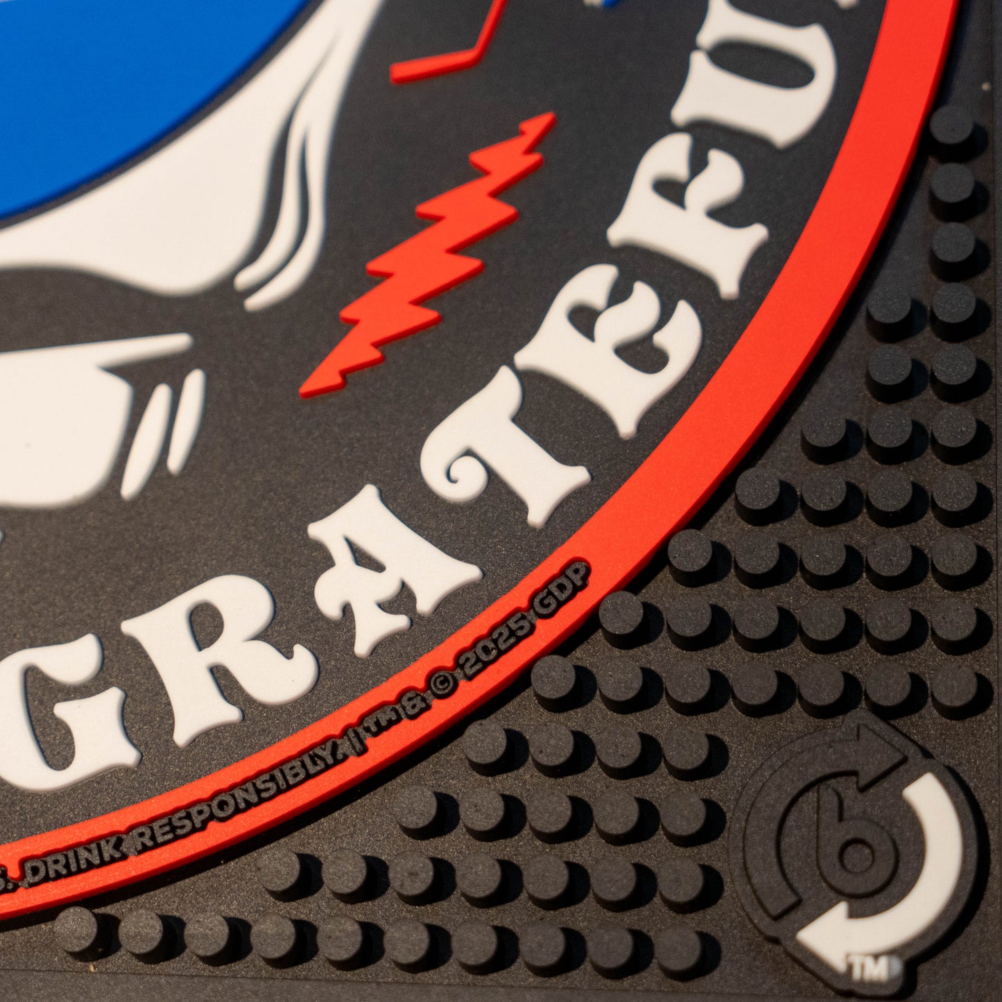 Close up of black square bar mat with a red, white, and blue Dogfish Head x Grateful Dead Logo.