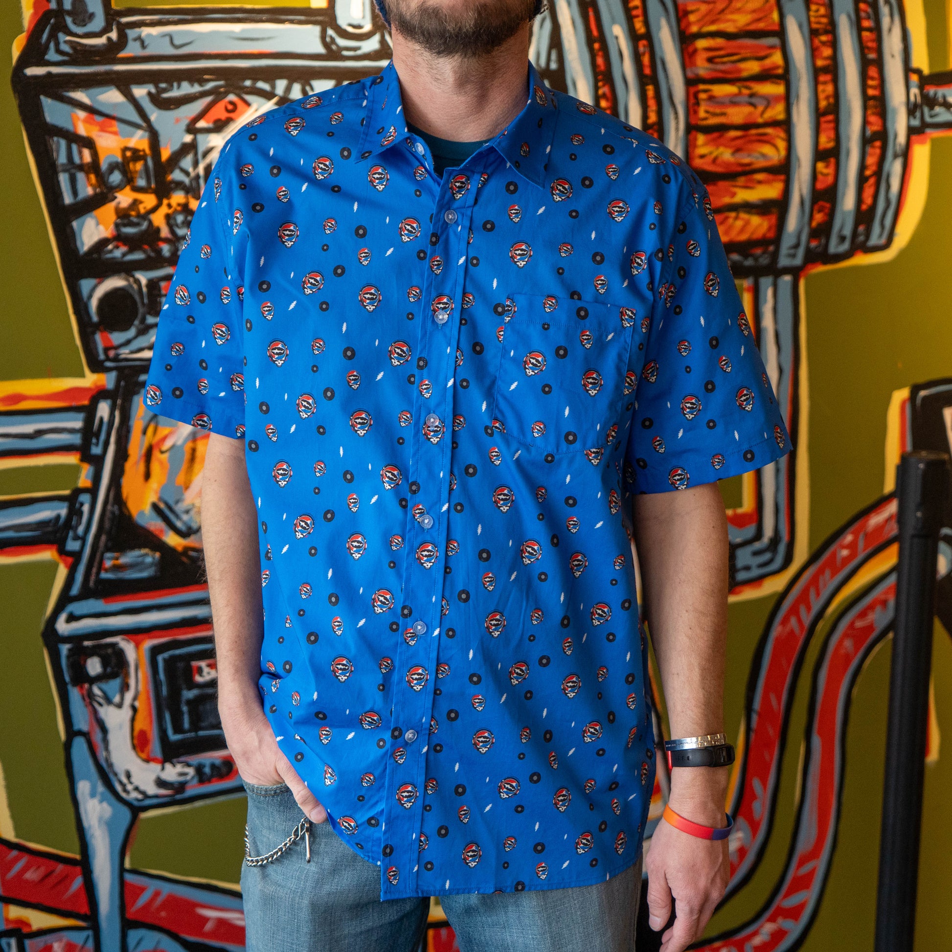 Man wearing a blue Dogfish Head x Grateful Dead button down shirt, designed in small lightning bolts, records, and Dogfish Head x Grateful dead red, white, and blue logos.