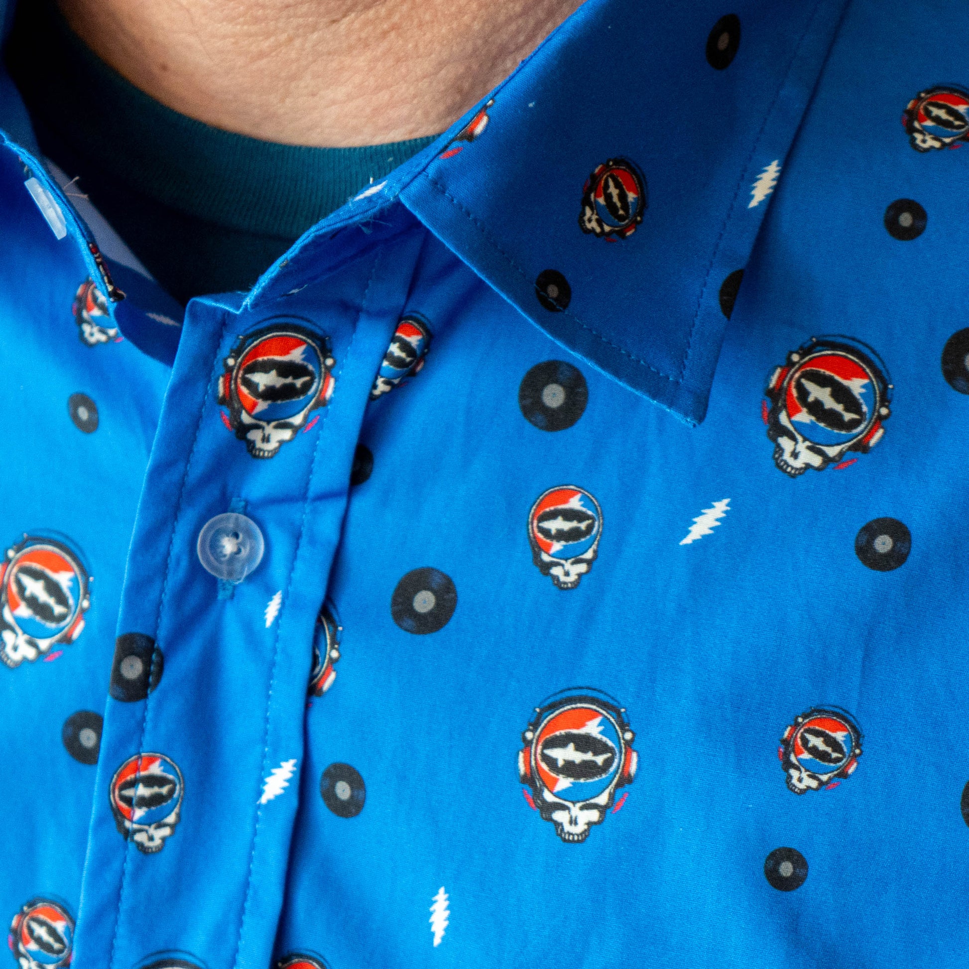 Close up of collar on blue Dogfish Head x Grateful Dead button-down shirt, designed in small lightning bolts, records, and Dogfish Head x Grateful dead red, white, and blue logos.