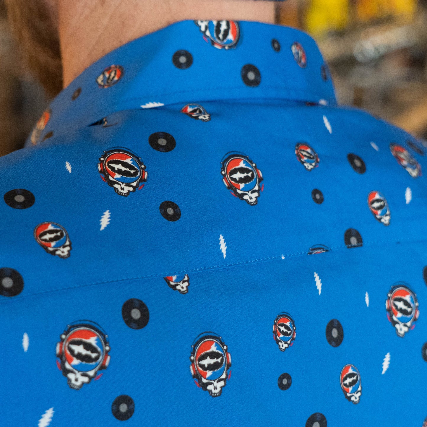 Close up of back collar on blue Dogfish Head x Grateful Dead button-down shirt, designed in small lightning bolts, records, and Dogfish Head x Grateful dead red, white, and blue logos.