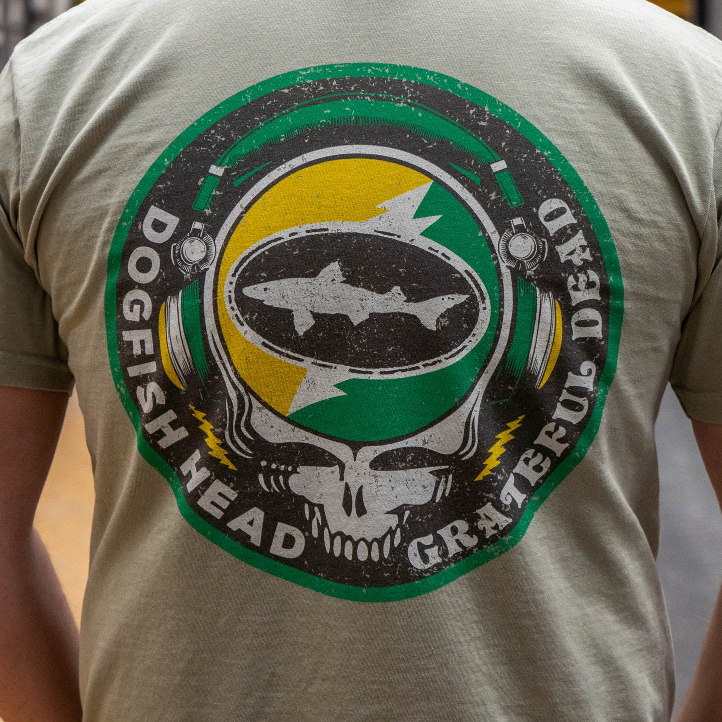 Close up of the backside of Dogfish Head x Grateful Dead Citrus Daydream Short Sleeve Sand colored tee, showing a large Dogfish Head x Grateful Dead Logo in citrus orange and Dogfish Head green. 