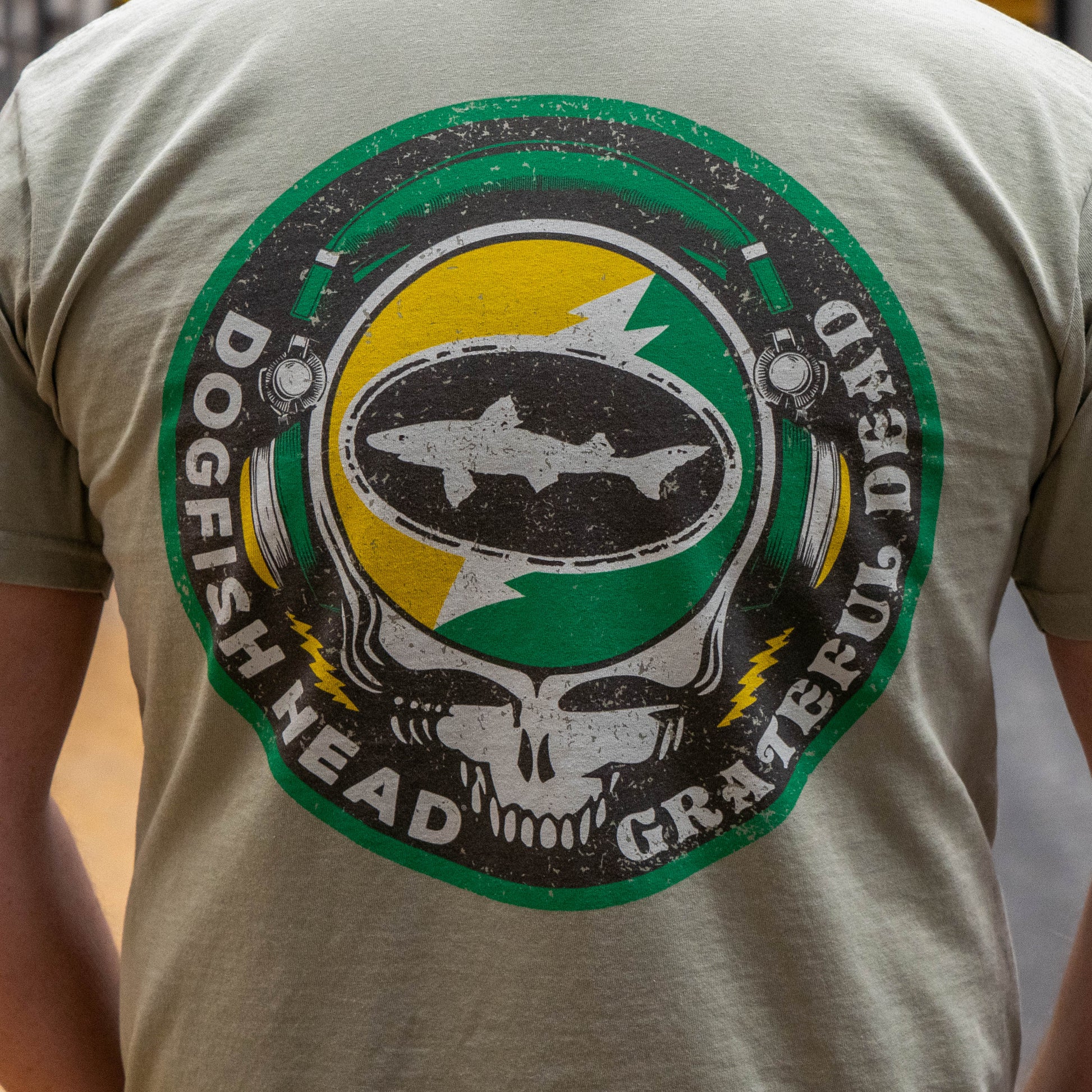 Close up of the backside of Dogfish Head x Grateful Dead Citrus Daydream Short Sleeve Sand colored tee, showing a large Dogfish Head x Grateful Dead Logo in citrus orange and Dogfish Head green. 