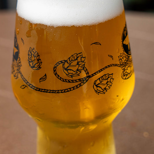 An Anchor IPA Glass filled with golden beer and foam, featuring a black printed design of a rope entwined with hop cones.