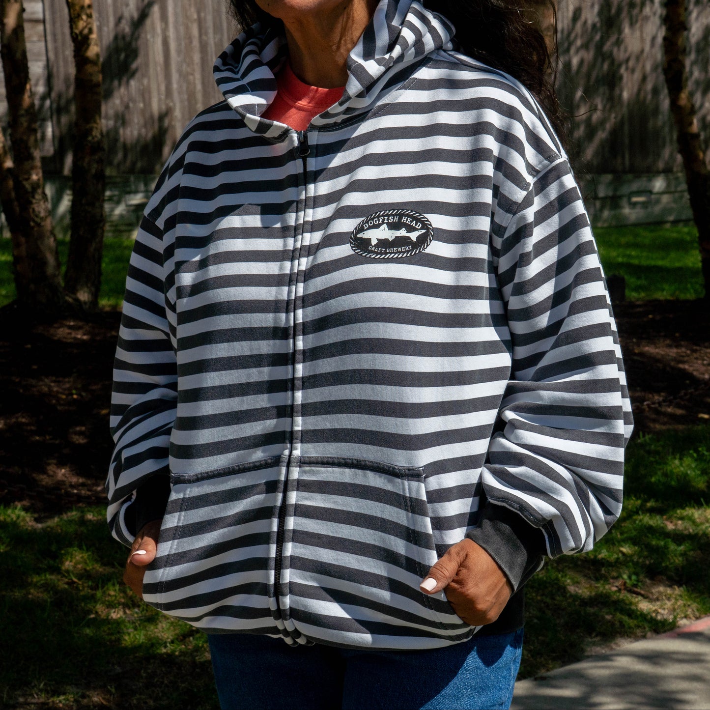A person outdoors wearing a zip-up hoodie with horizontal black and white  stripes, a shark graphic on the chest, and a red shirt underneath.