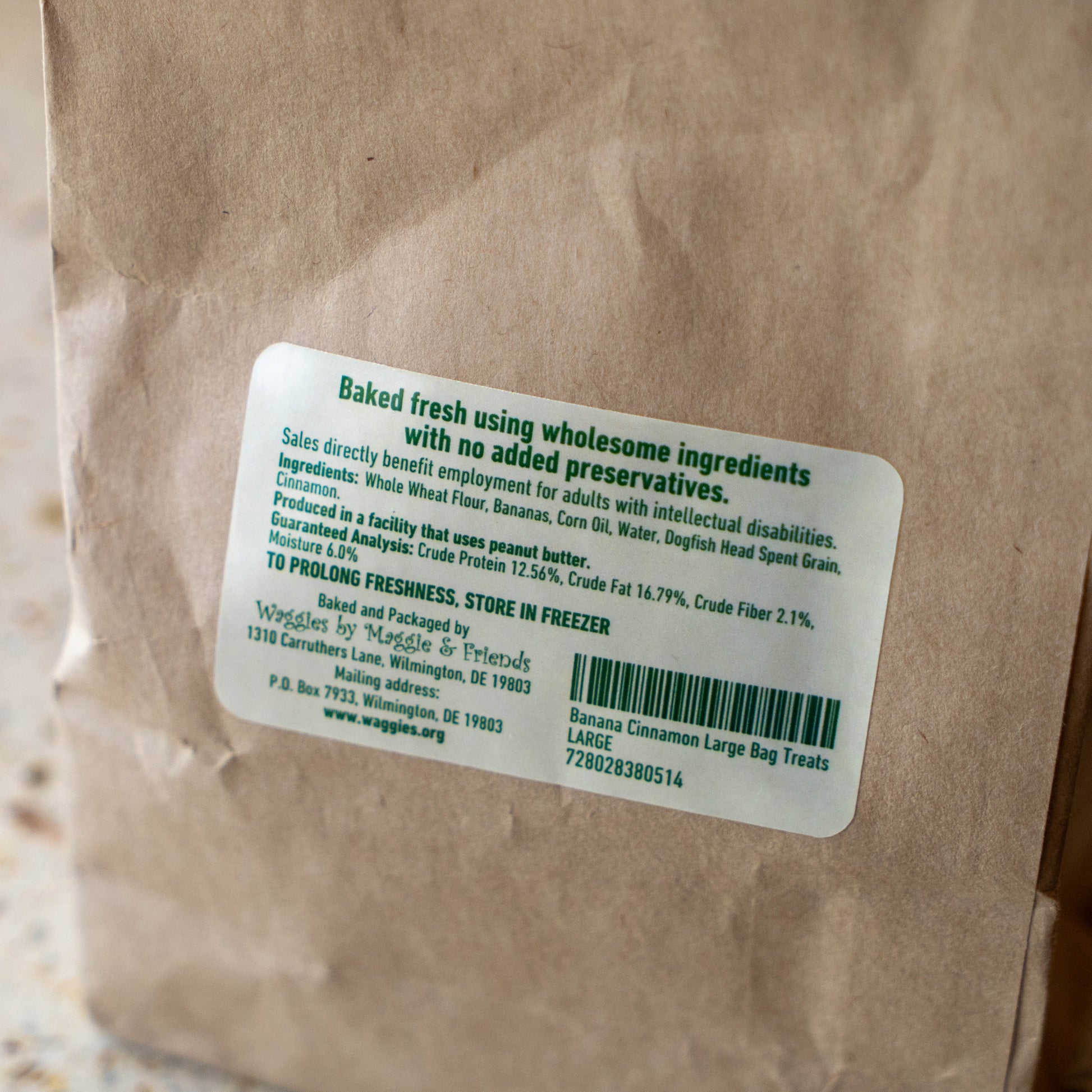 A close-up of a brown kraft paper bag with a white product label. The label reads 'Baked fresh using wholesome ingredients with no added preservatives.