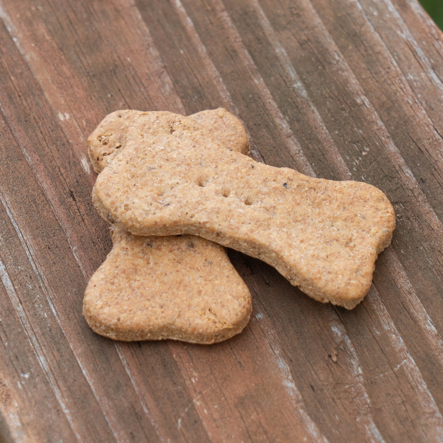 Two bone-shaped dog treats stacked on a rustic wooden surface.