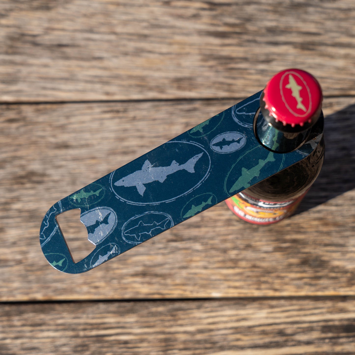 Shark-patterned bottle opener on a wooden surface with a bottle.