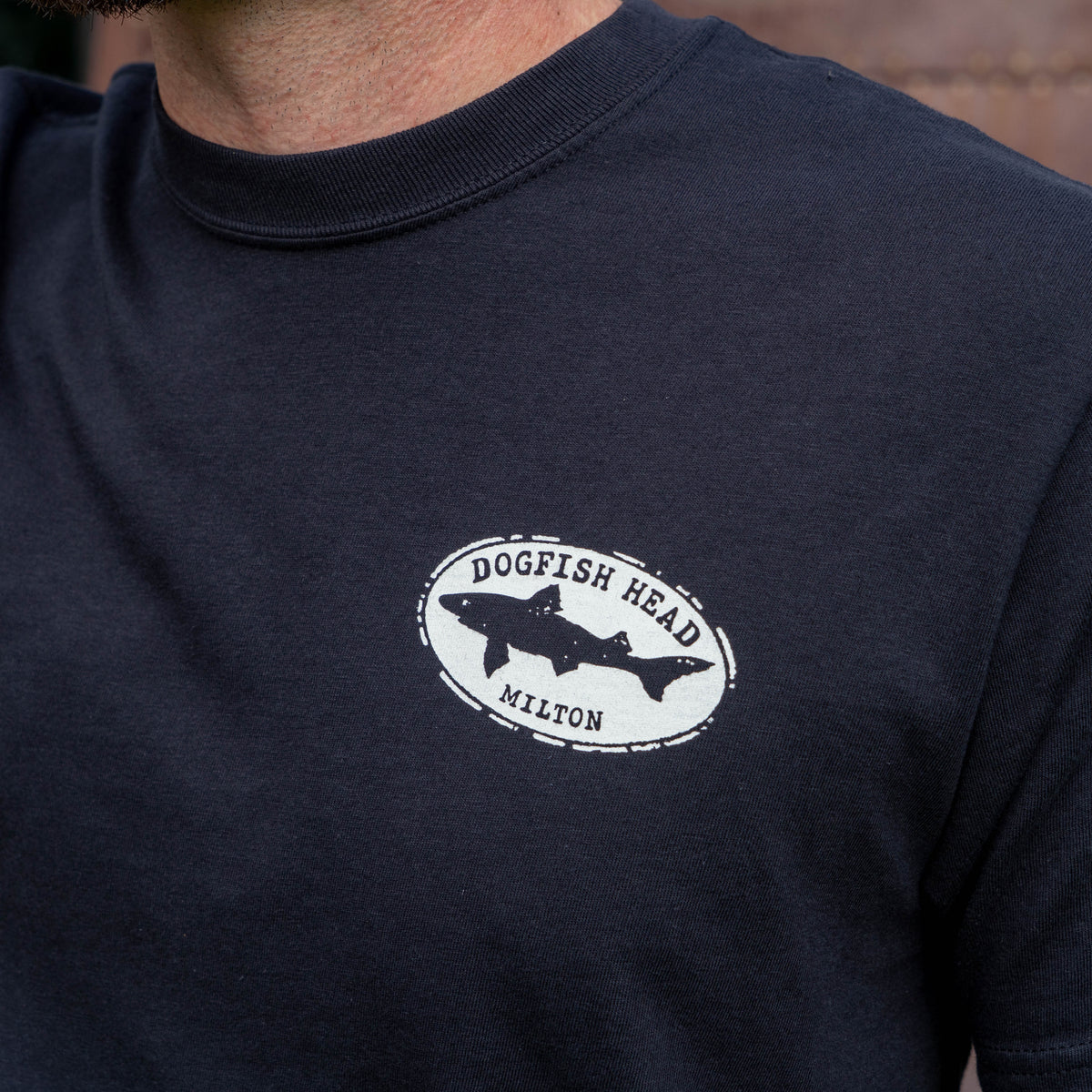 Male standing with arm outward.  Wearing black tee shirt that says 'dogfish head  Milton'