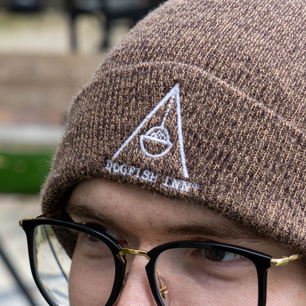 A person wearing a brown marled Firepit Beanie embroidered with a white triangular logo above the text DOGFISH INN.
