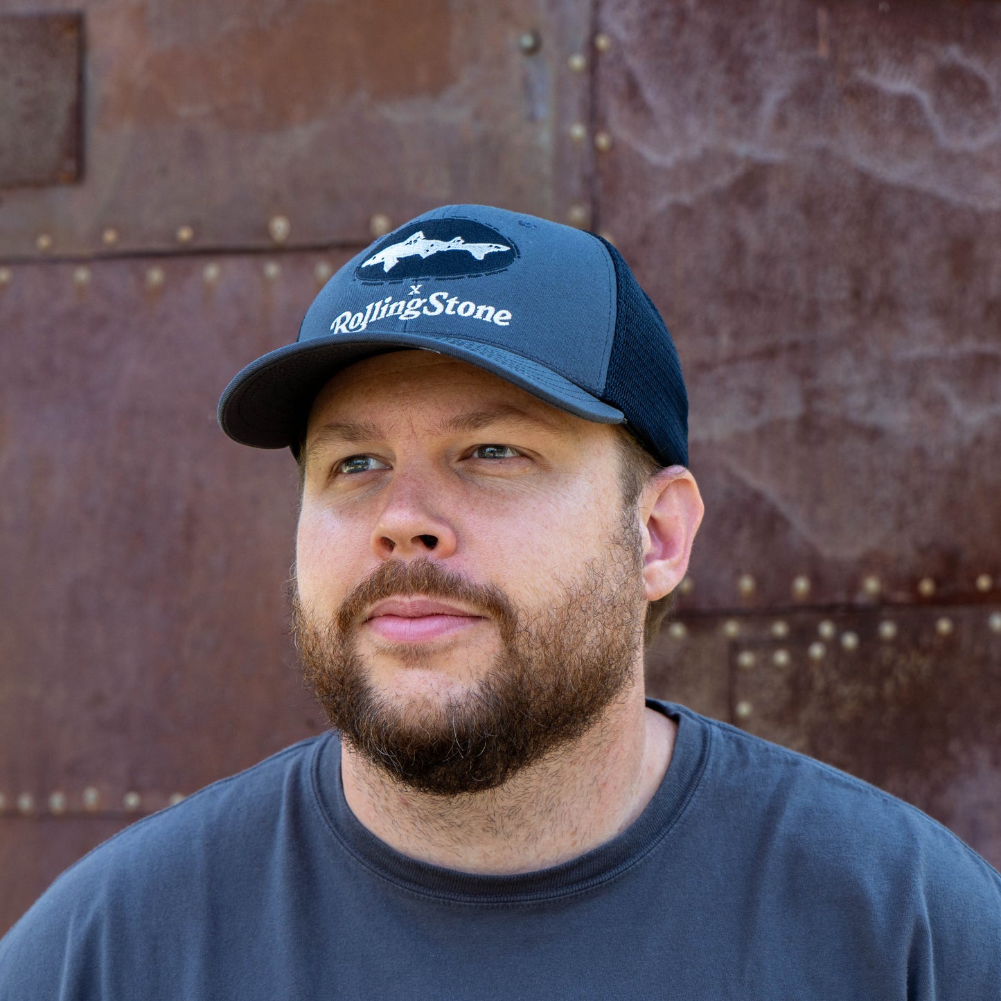 Man wearing a navy cap with a Dogfish Head x 'Rolling Stone' logo against a textured brown background