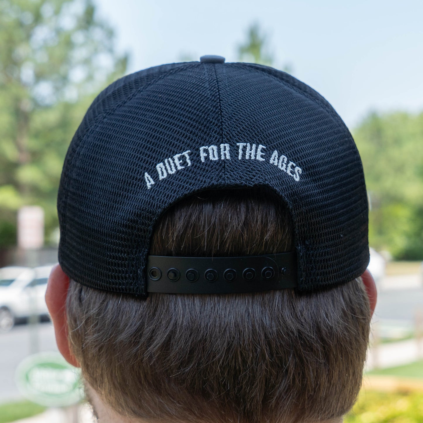Black mesh cap with 'A Duet For The Ages' text on the back, worn by a person outdoors.