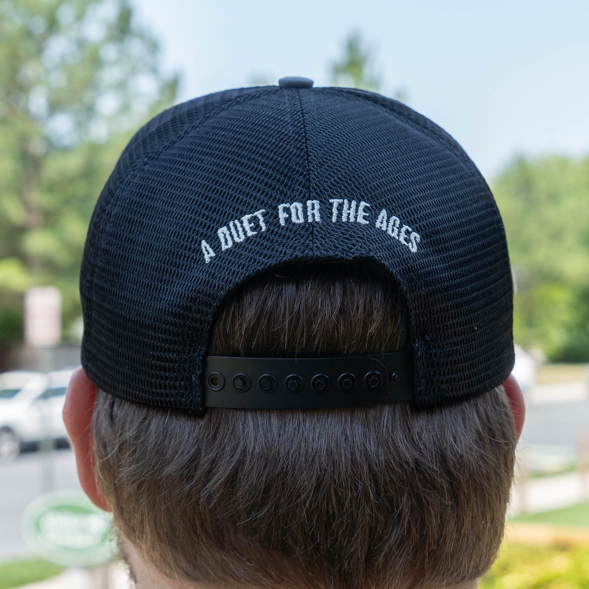 Black mesh cap with 'A Duet For The Ages' text on the back, worn by a person outdoors.
