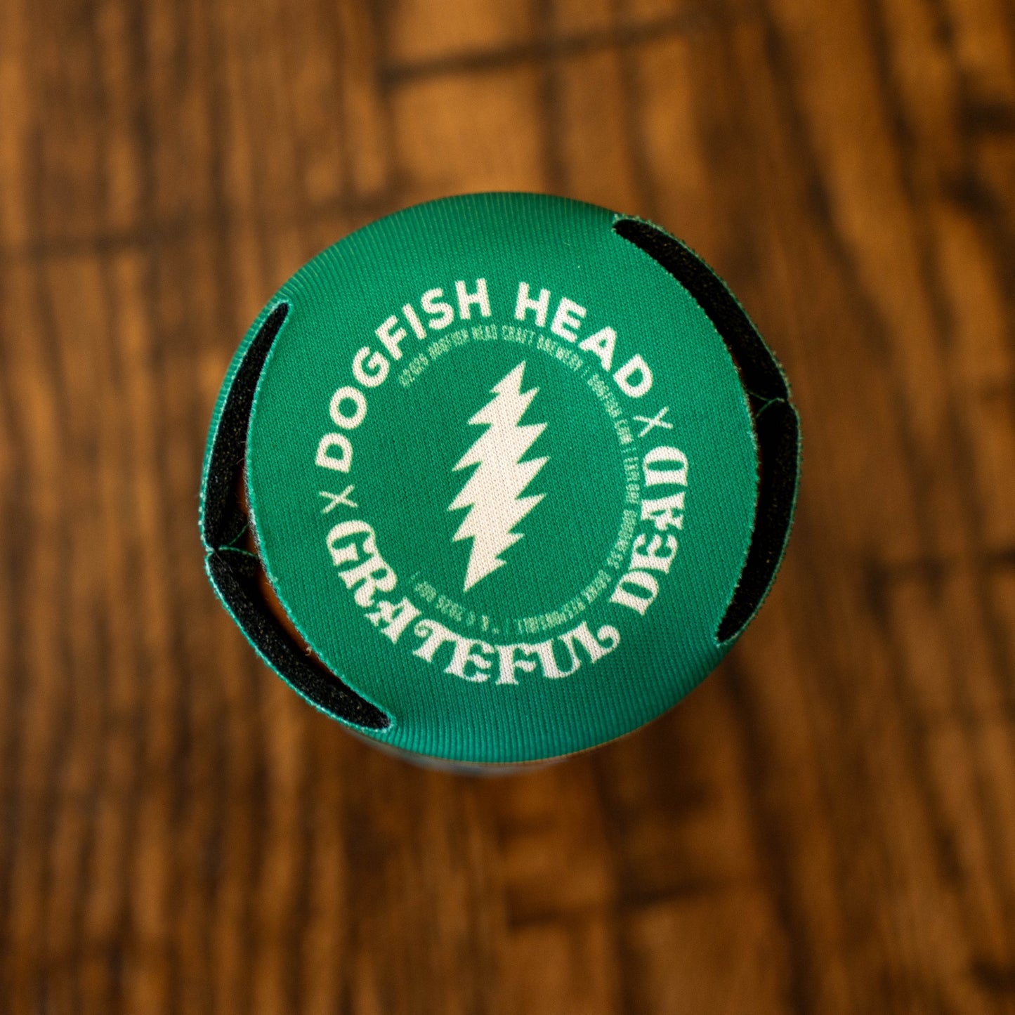 A Dogfish Head bottle cap featuring the Grateful Dead logo sits on wood—an ideal match for the Dogfish Head x Grateful Dead Citrus Daydream 12oz Can Cooler by Grandstand Glassware & Apparel, perfect for fans of both brands.