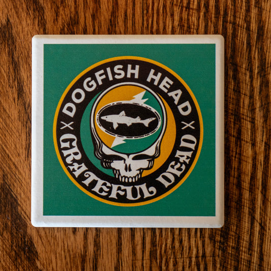 The Dogfish Head x Grateful Dead Citrus Daydream Ceramic Coaster by Paint the Town, Inc. features a fish inside a skull, lightning bolt, and circular text, blending both logos on a square ceramic coaster set atop wood.