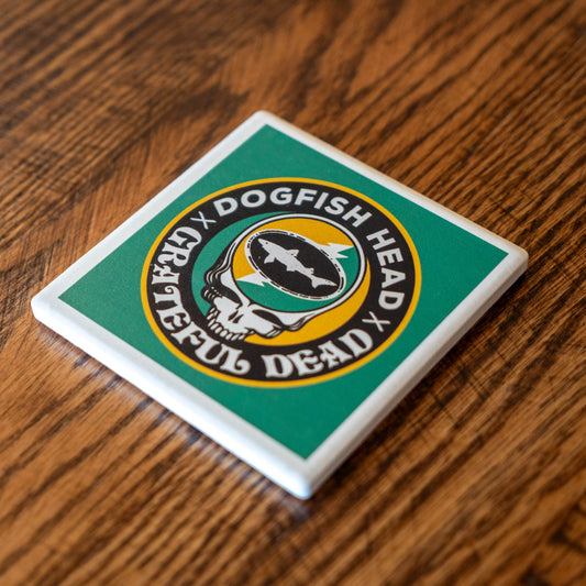 The Dogfish Head x Grateful Dead Citrus Daydream Ceramic Coaster by Paint the Town, Inc. features a green background with the brewery logo and iconic Grateful Dead skull, displayed on a wooden surface.