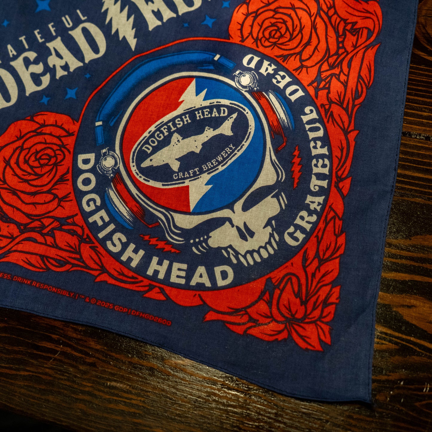 Close up of Dogfish Head X Grateful Dead Logo. Skull is in red, white, and blue and is wearing a pair of headphones. In the center of Grateful Dead skull is the lightning bolt striking through the Dogfish Head Craft Brewery logo.