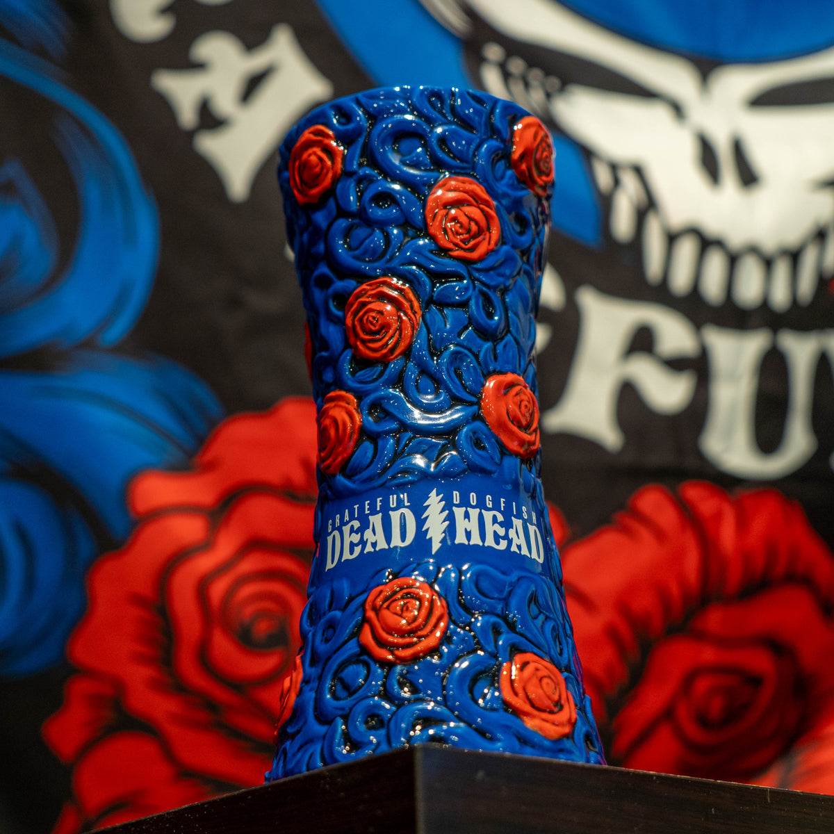 Blue ceramic Dogfish Head x Grateful Dead TIKI FARM Ceramic Mug decorated with red roses and embossed text reading Grateful Dead Dogfish Head with a lightning bolt symbol.