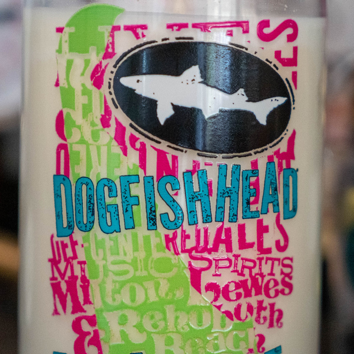 Delaware Grunge Can Glass Candle in a glass jar featuring a screen-printed shark icon, blue Dogfish Head text, and layered pink and green lettering reading Milton, Rehoboth, Spirits, and Brewes.
