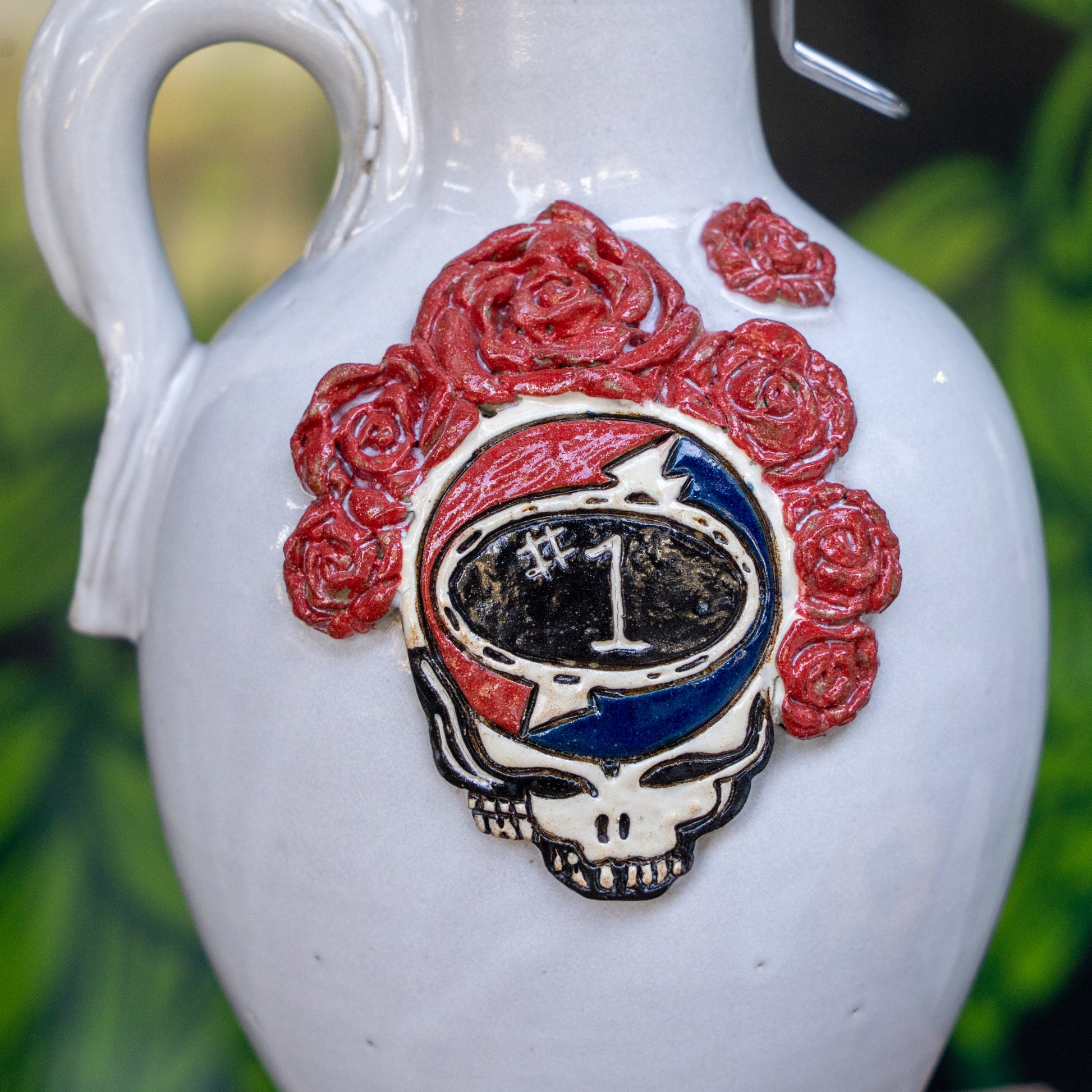 The Uber Growler by Romanick Pottery is a handmade white ceramic growler featuring a relief of a skull, lightning bolt, roses, and “#1” in the center—Grateful Dead-inspired and perfect as a unique holiday gift.