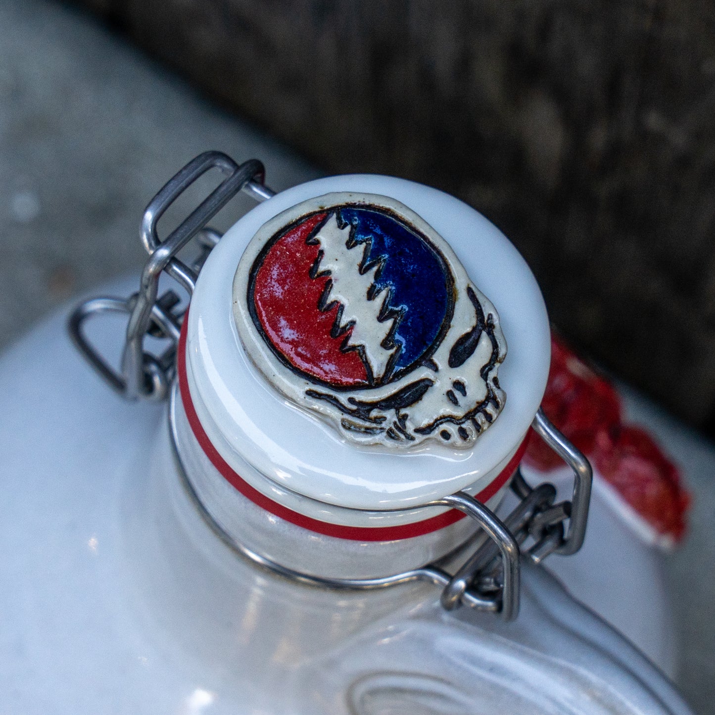 A close-up of the Uber Growler by Romanick Pottery, featuring a ceramic stopper with the Grateful Dead "Steal Your Face" skull in red, white, and blue, plus a metal clasp and wax seal for a handmade, unique look.