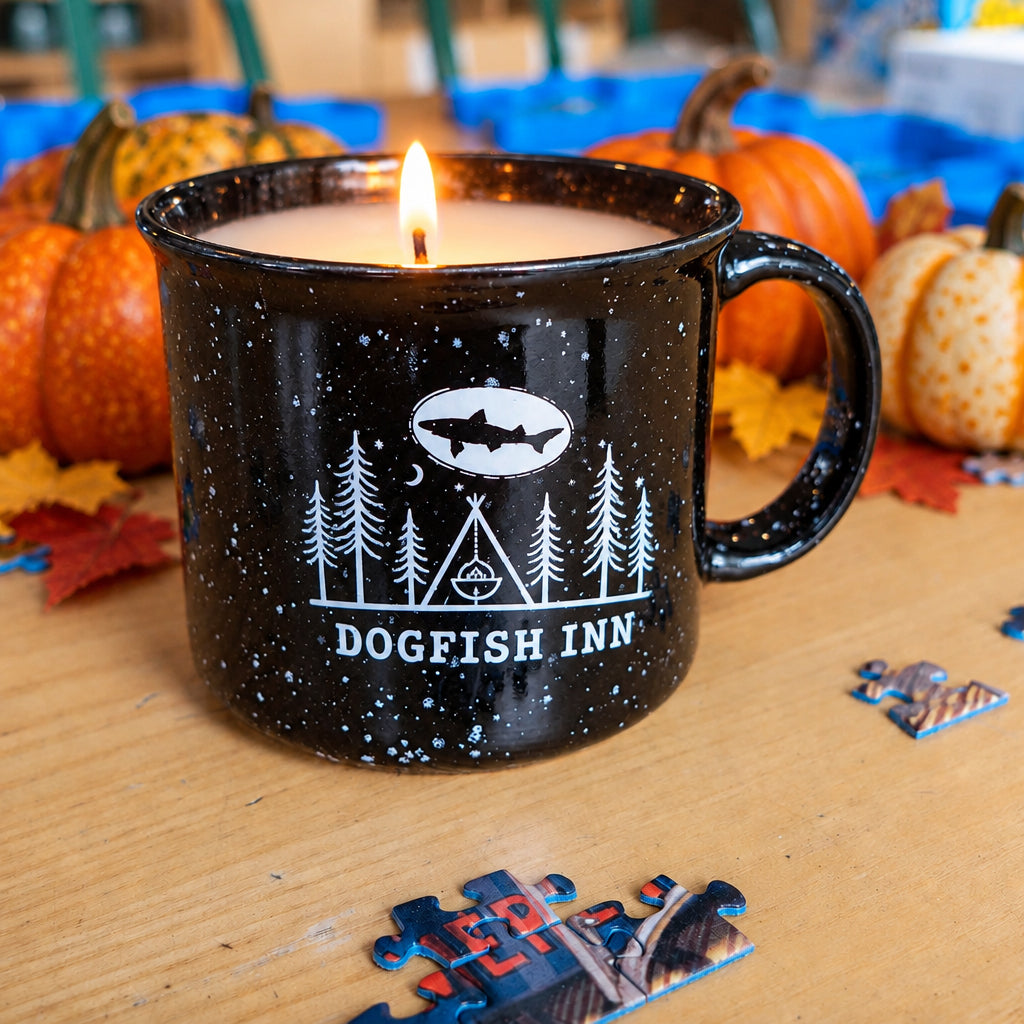Black speckled ceramic mug with white artwork on front says 'dogfish inn' sittting on table with puzzle pieces.