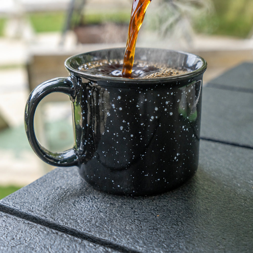 Hot coffee being poured into black speckled mug sitting on coffee table.