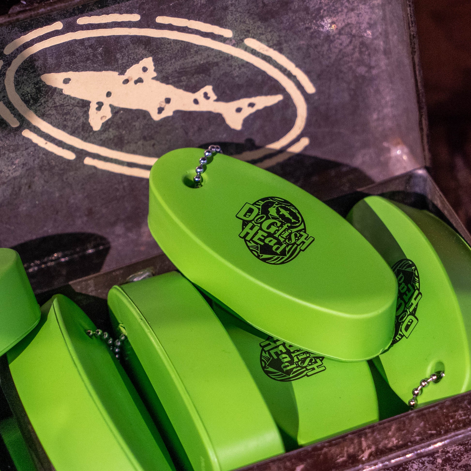 Bright green oval-shaped DGI Health keychain flossers with metal ball chains, displayed inside a dark metal tin with a shark logo on the lid.