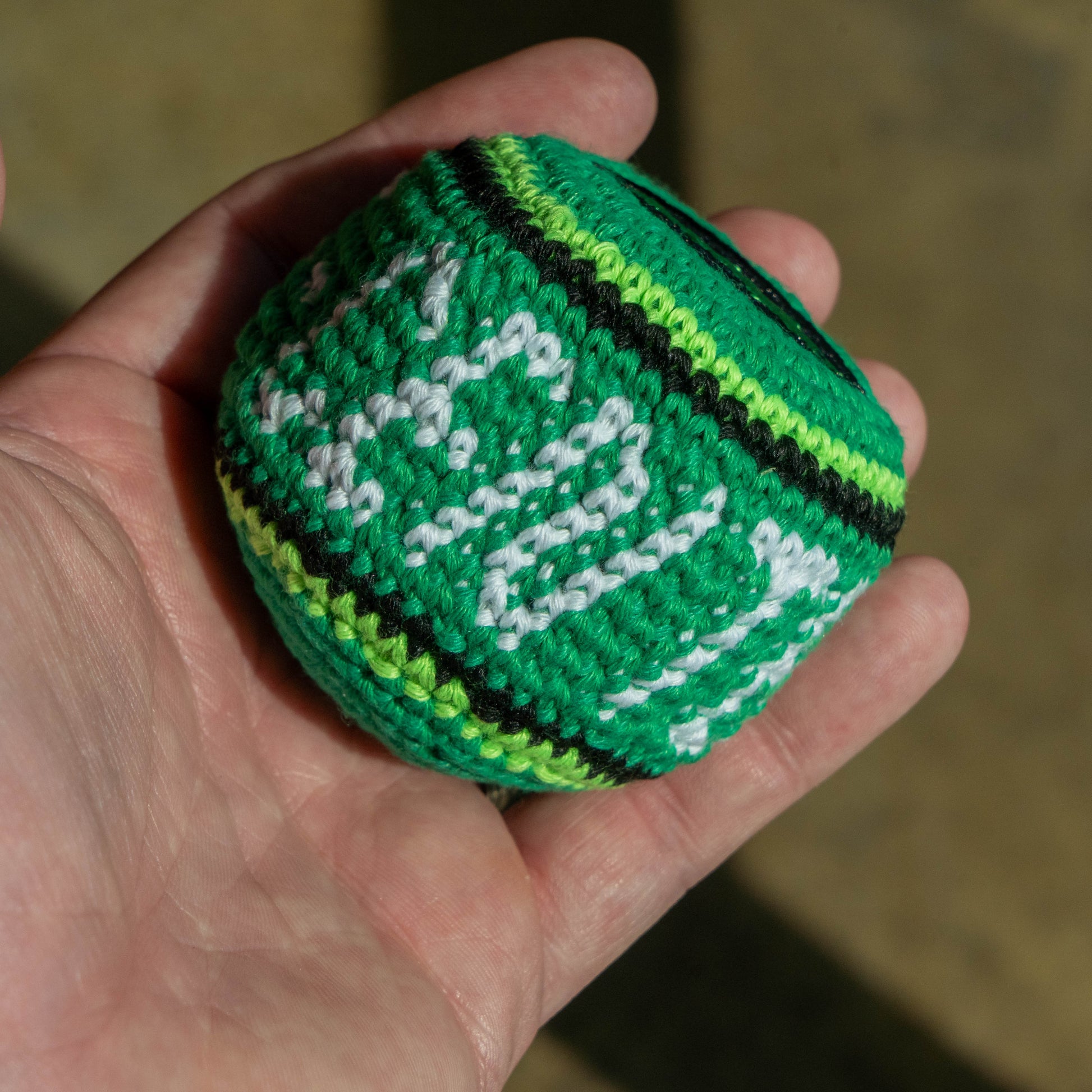 A hand holding a small green crocheted ball with white and black patterns.