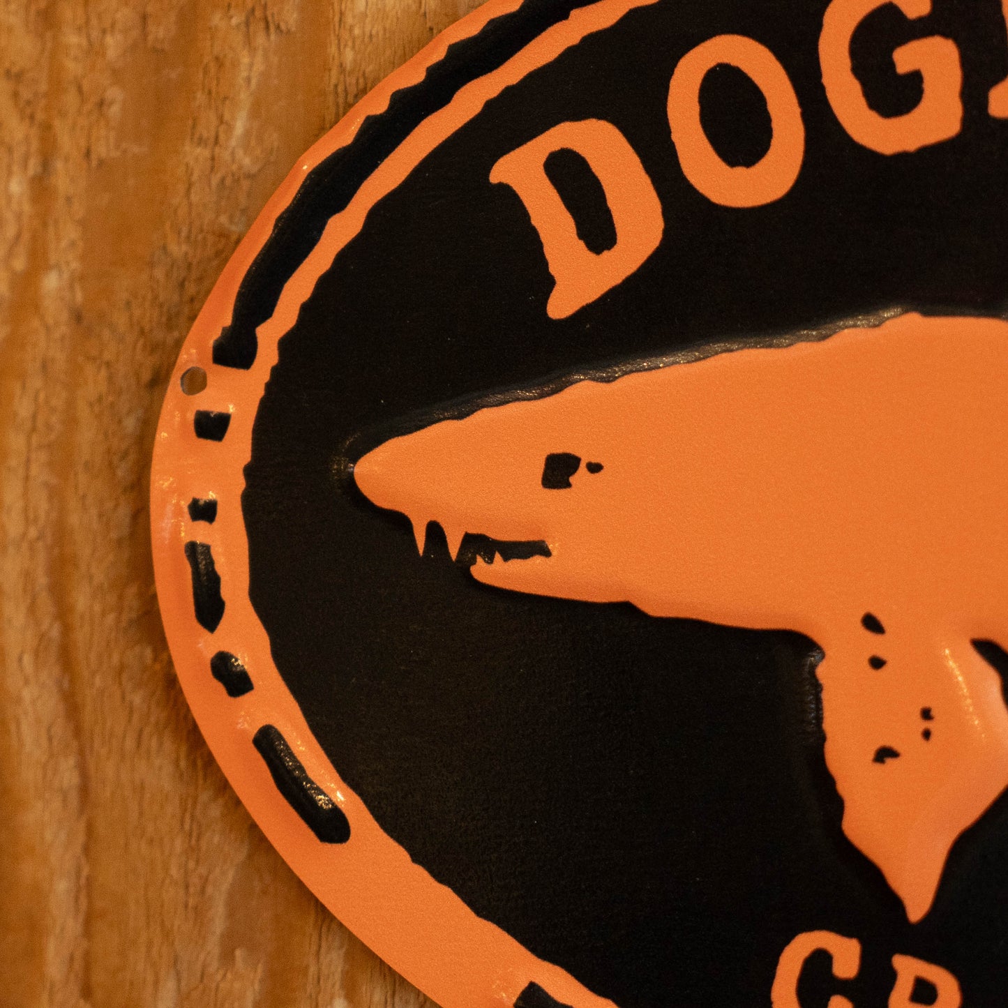 A close-up of a circular black and orange metal sign featuring a stylized dog head silhouette and the partial text 'DOG' on a wooden surface.