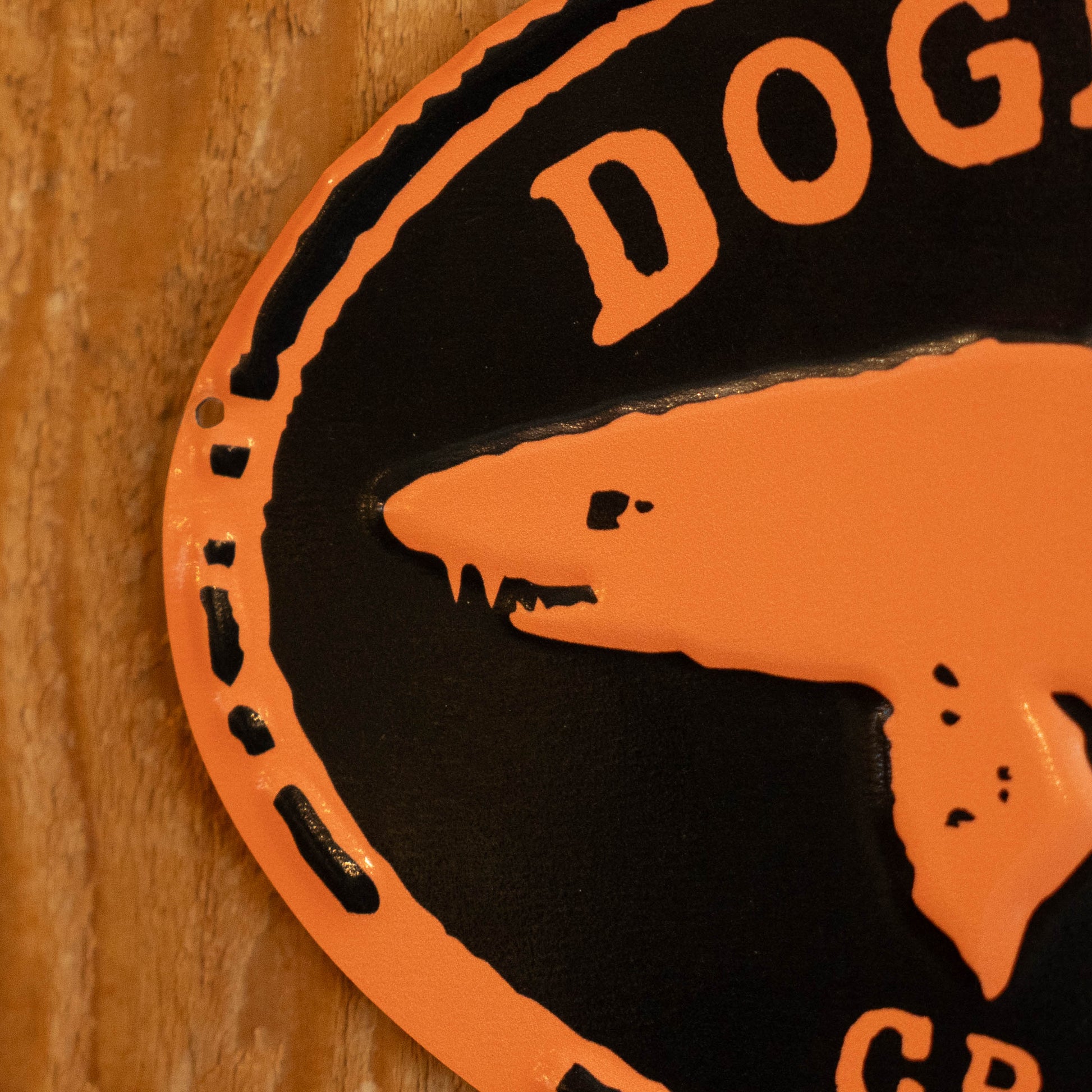 A close-up of a circular black and orange metal sign featuring a stylized dog head silhouette and the partial text 'DOG' on a wooden surface.