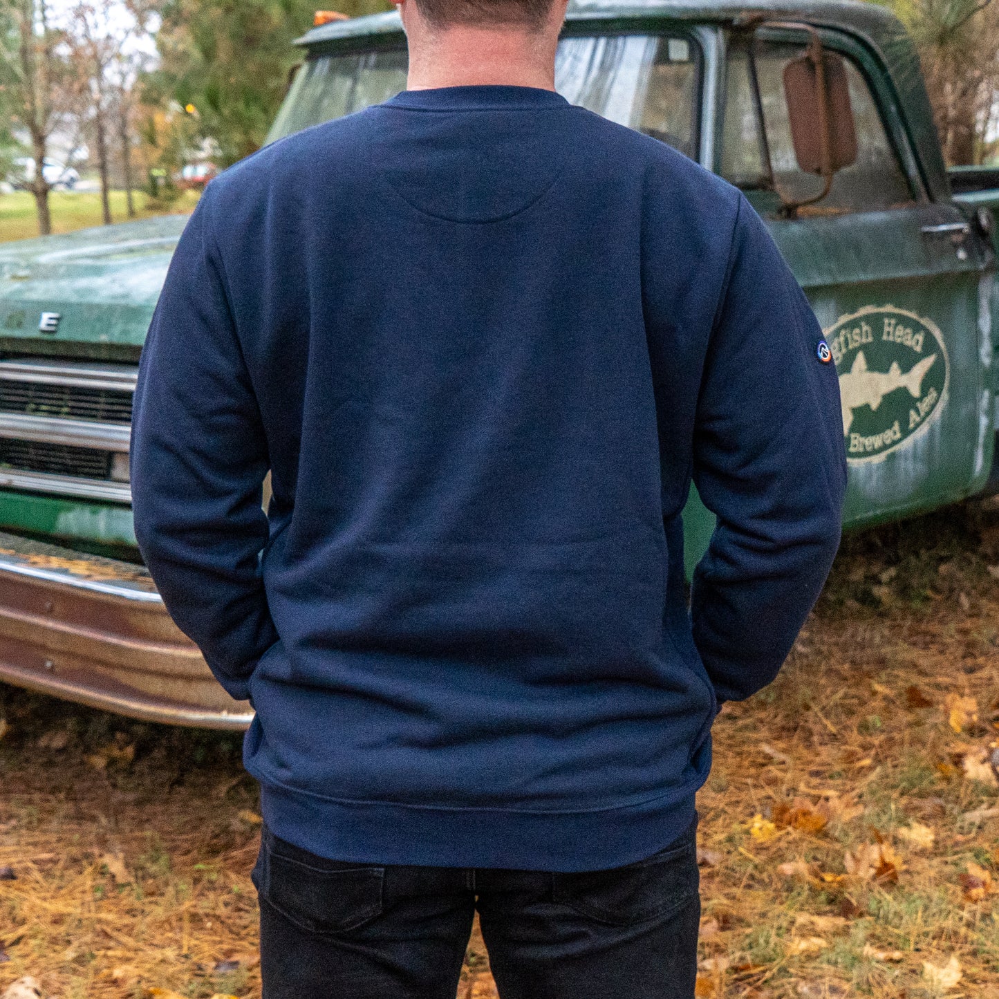 Person wearing a navy blue sweatshirt with a logo in front of an old green truck.