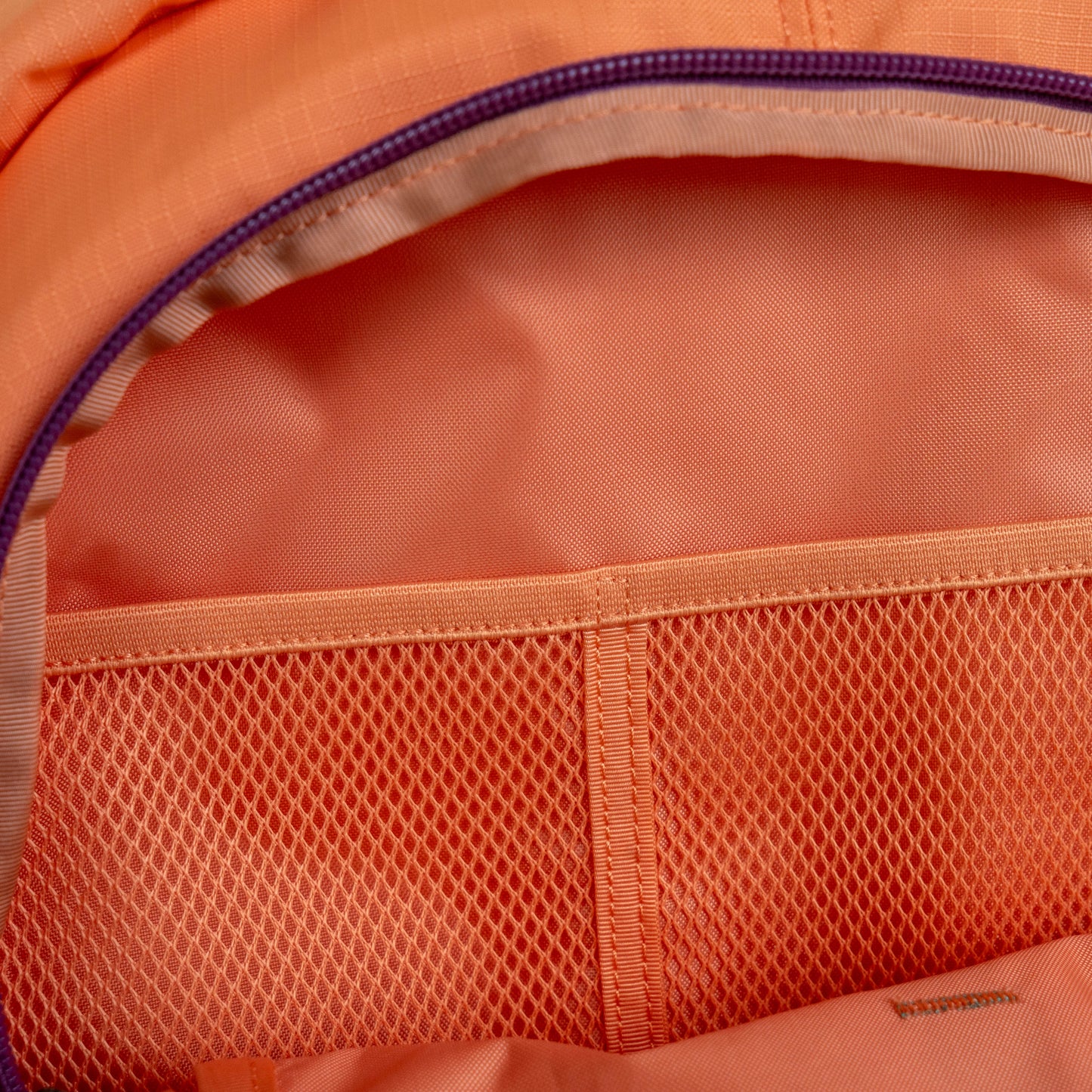 Interior detail of Patagonia Refugio 26L backpack showing mesh organizer pocket, zippered compartment, and durable recycled ripstop lining in coral color for everyday carry and travel use