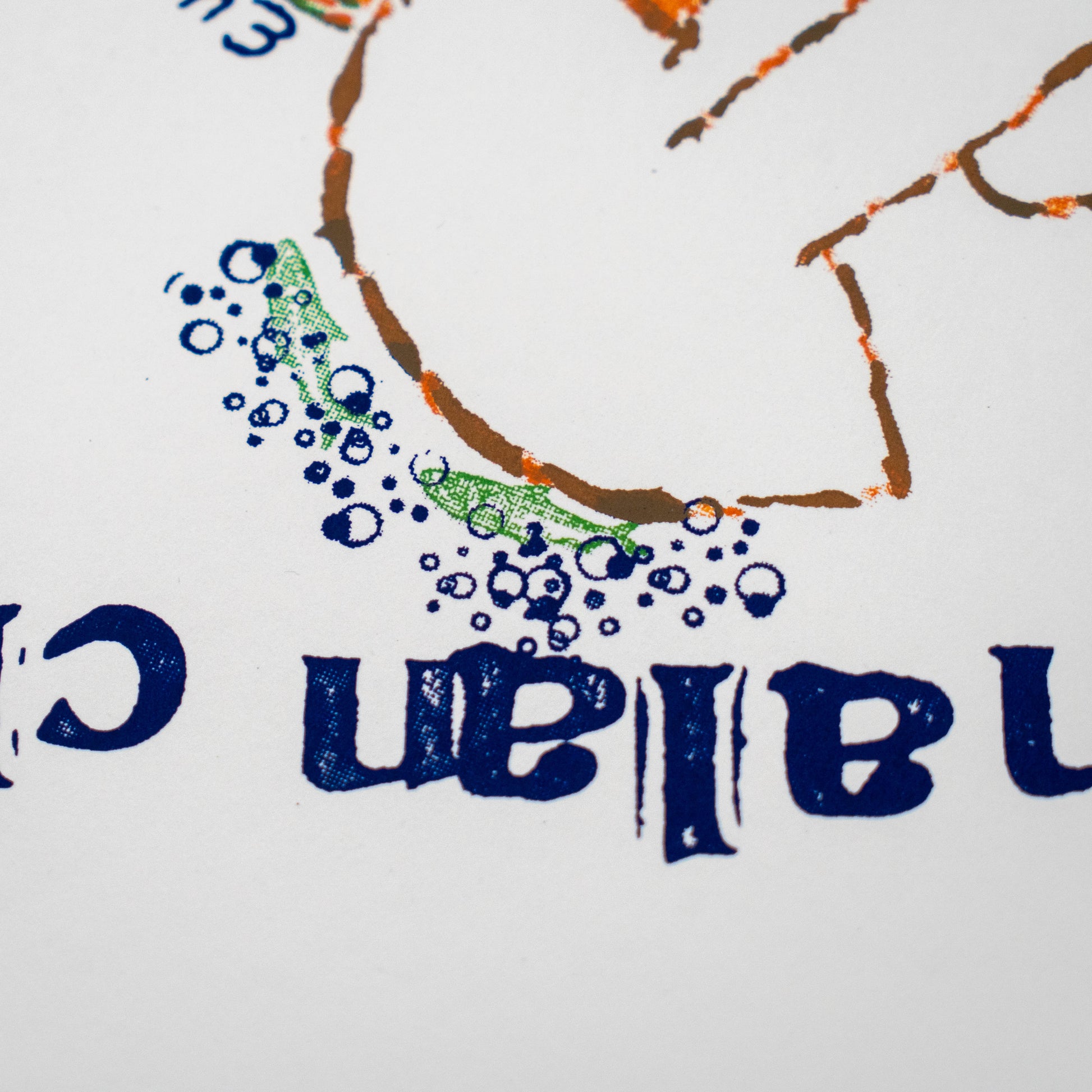 Close-up of a printed graphic on white paper, showing blue mirrored lettering, a brown outlined shape, green scribbled marks, and blue bubble-like dots.