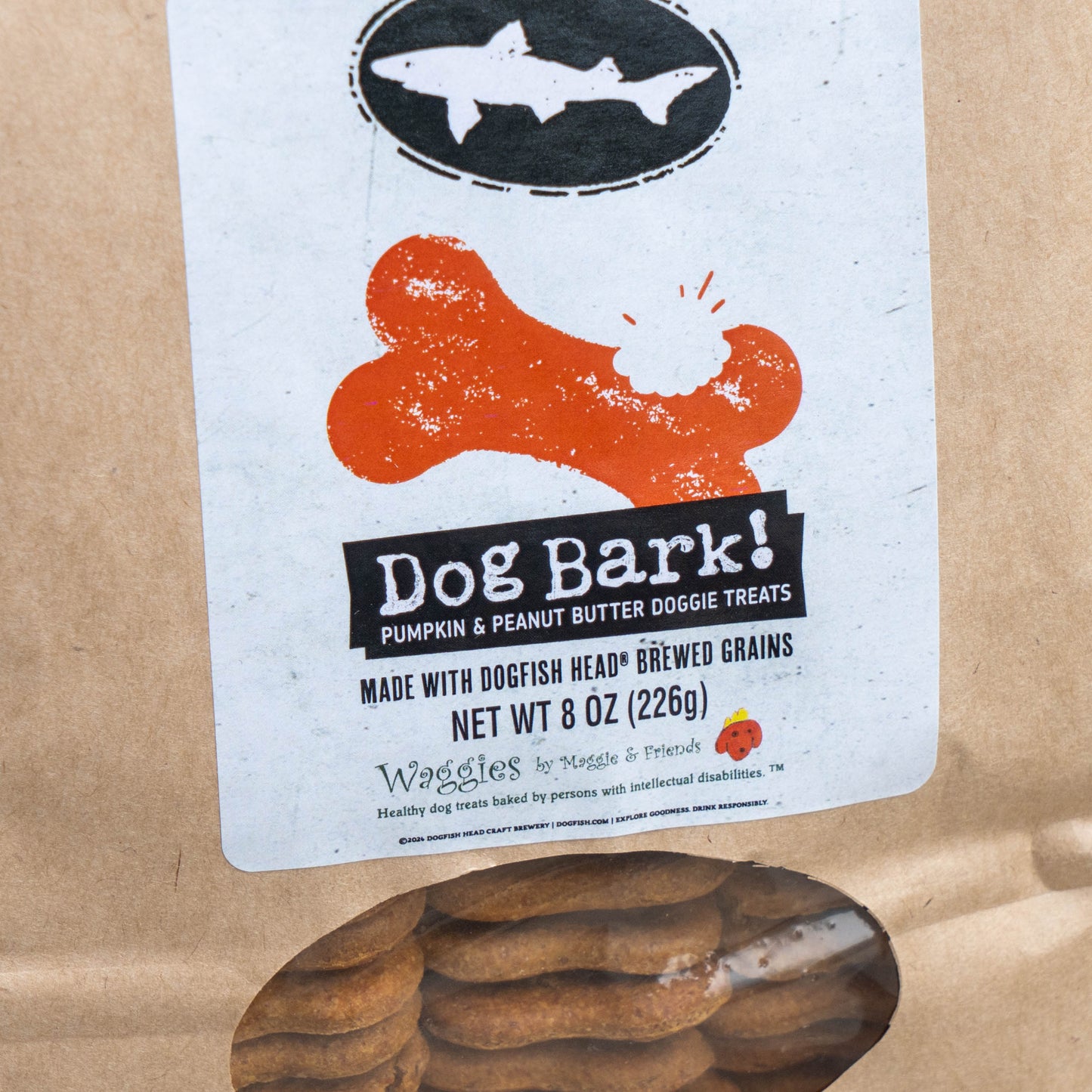 A kraft paper bag of Waggles to Dogs & Friends Dog Bark! dog treats, showing a white label with a black fish logo and orange bone graphic, with treats visible through a clear window at the bottom.