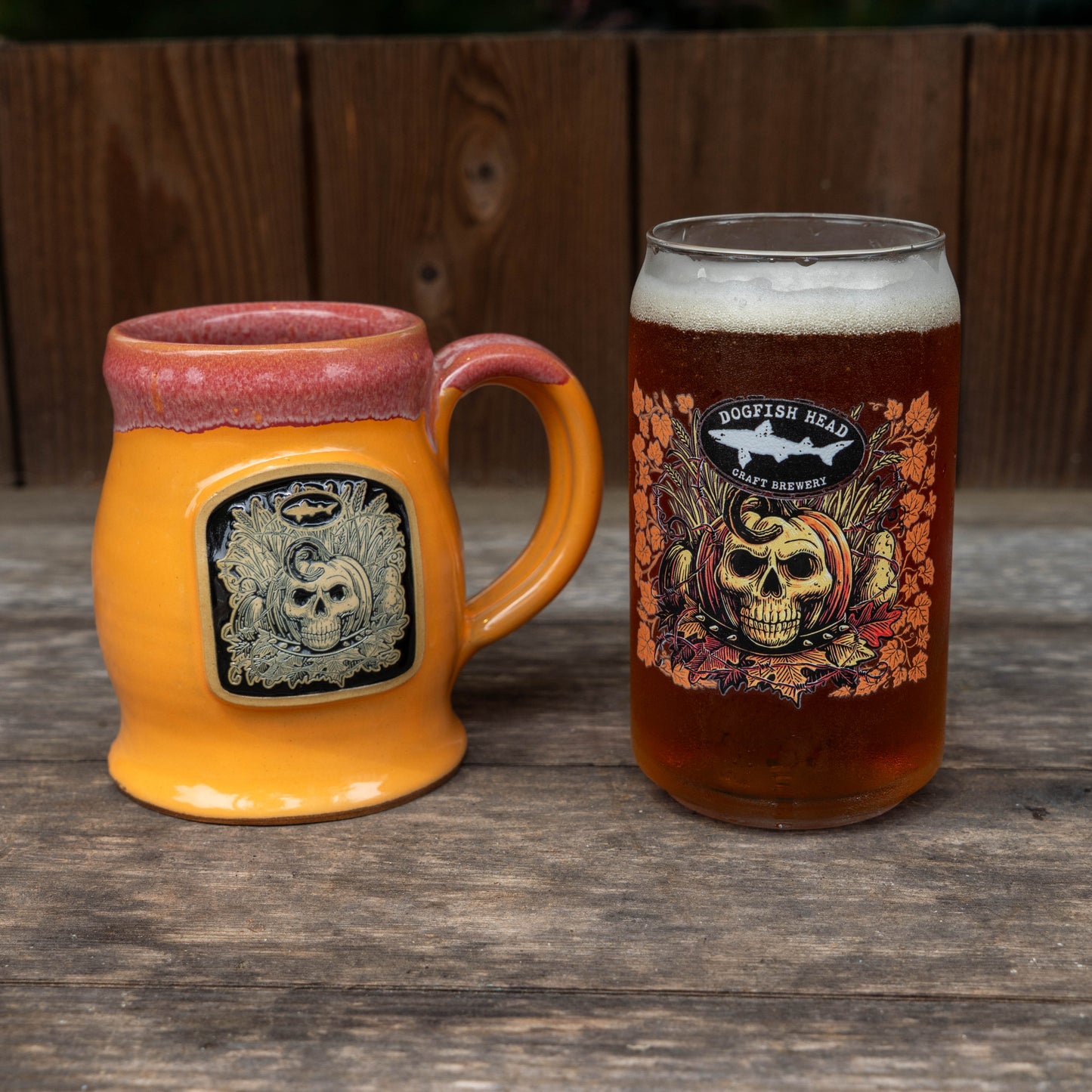A ceramic orange mug with a pink rim and a skull graphic, next to a glass of amber beer with a 'Dogfish Head Craft Brewery' skull label, set on a rustic wooden table.