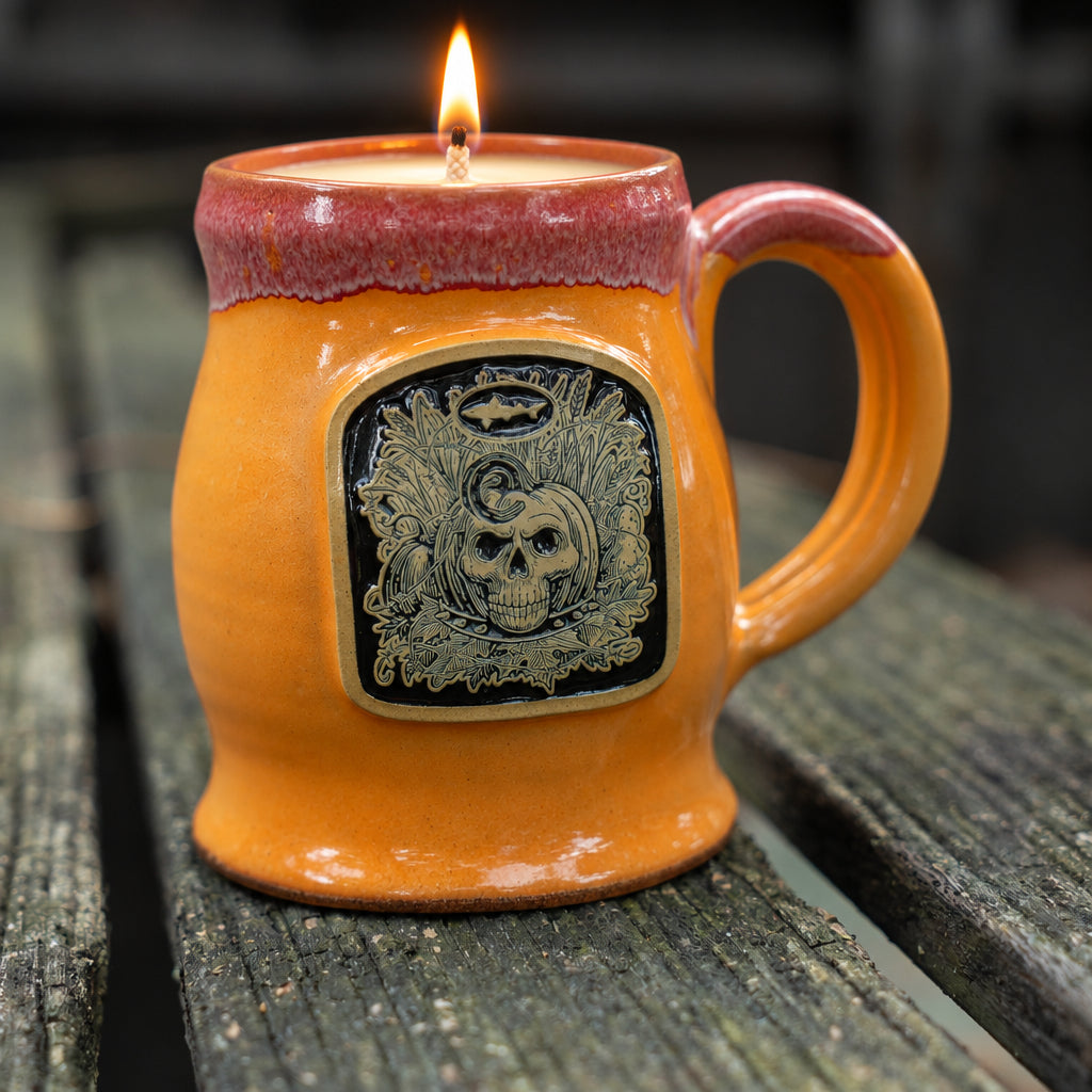 Orange ceramic mug with skeleton medalliion on the front with black fill.  Sitting on wooden table.