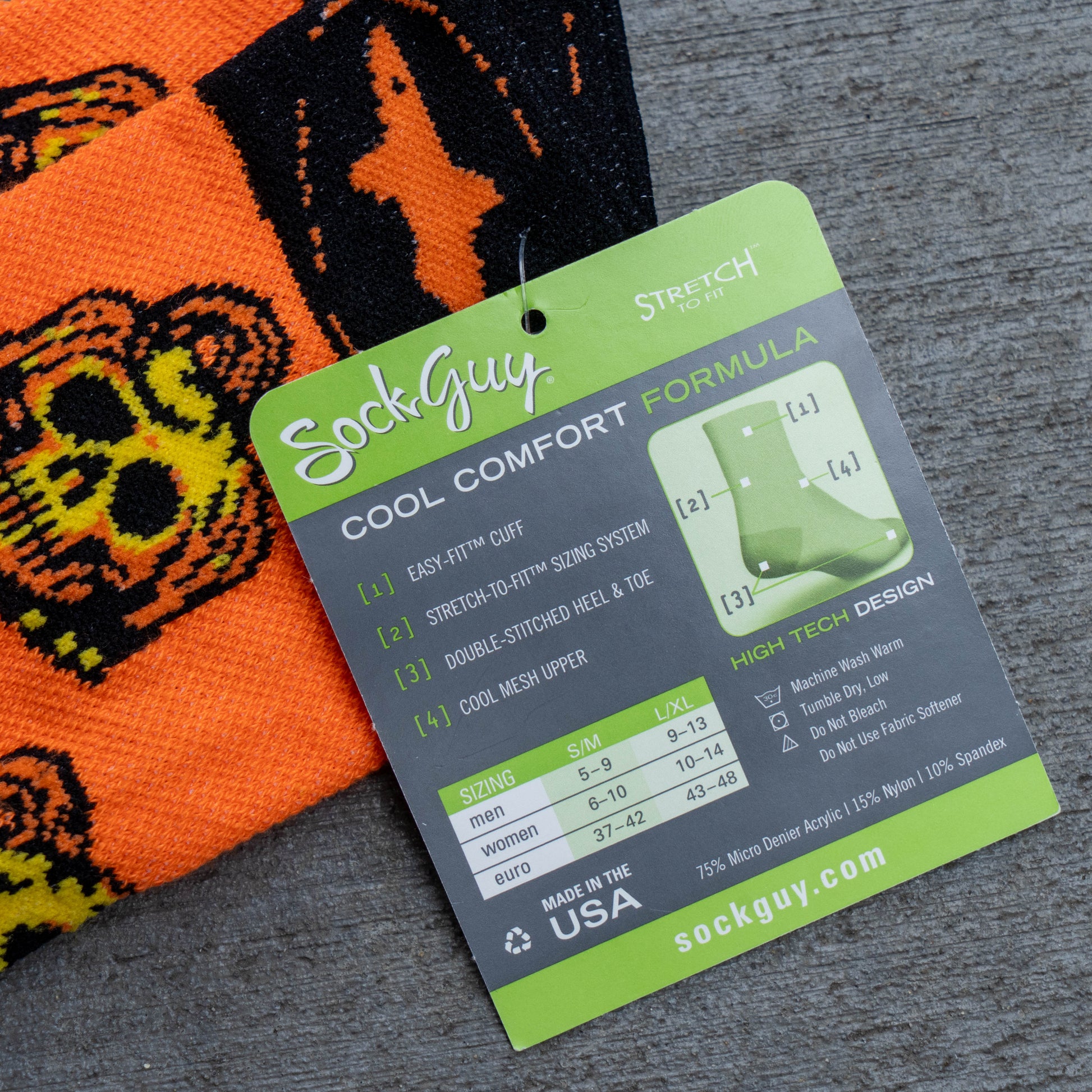 A close-up of a SockGuy sock tag card labeled 'Cool Comfort Formula' placed over an orange and black patterned sock on a gray textured surface.