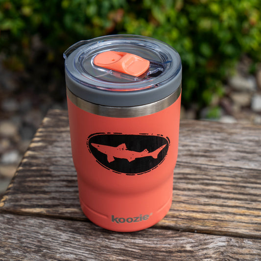 Salmon 12oz Can Insulator in salmon, a double-walled insulated cup with a clear plastic lid and a black oval emblem featuring a shark silhouette.
