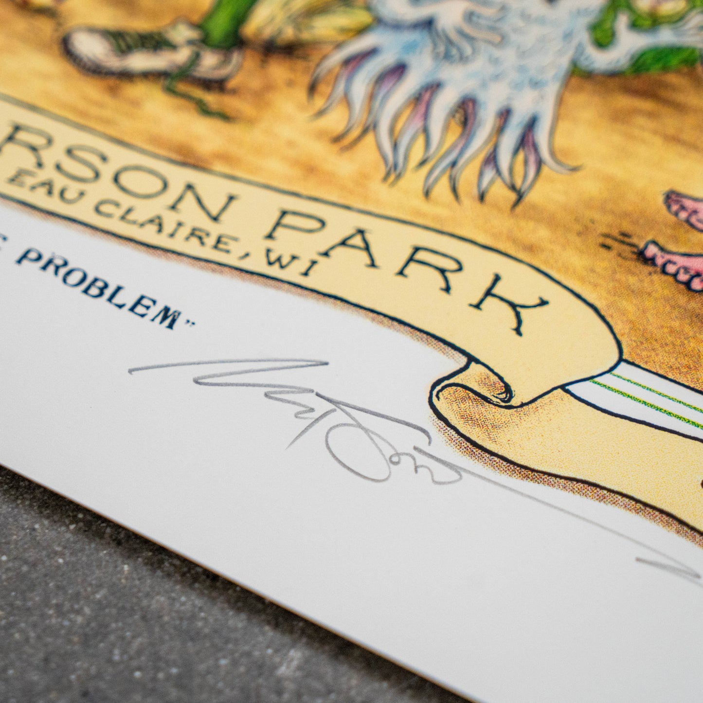 Close-up of the League Champions Limited-Edition Print by Marq Spusta, featuring part of an illustrated creature and the text “CARSON PARK EAU CLAIRE, WI” on a yellow banner, with Marq Spusta’s handwritten signature on the white margin.