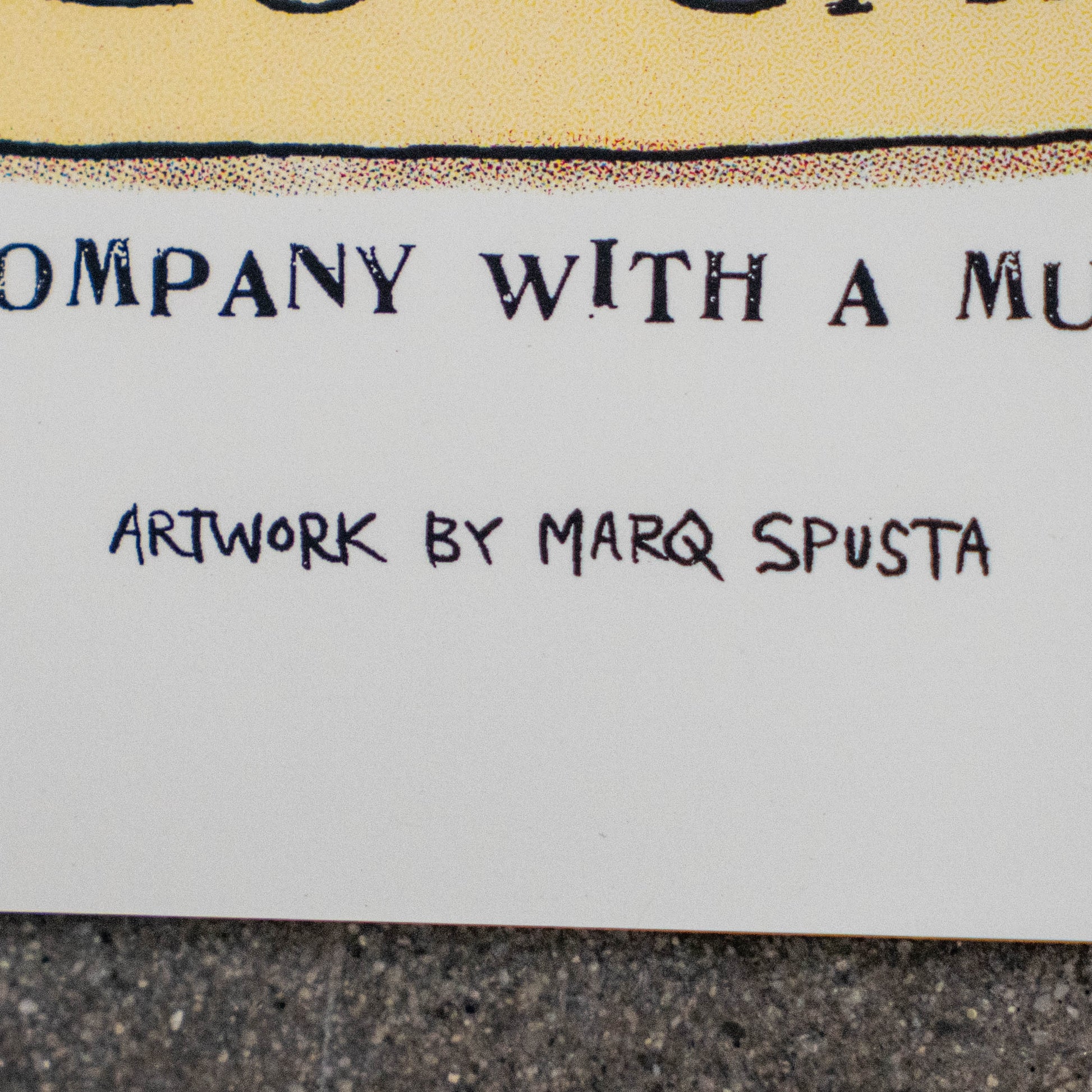 A close-up of text on the League Champions Limited-Edition Print by Marq Spusta reads, ARTWORK BY MARQ SPUSTA. The background features a portion of a word in bold, serif lettering and showcases a textured surface beneath, reflecting the distinctive style characteristic of Marq Spusta’s collaborations.