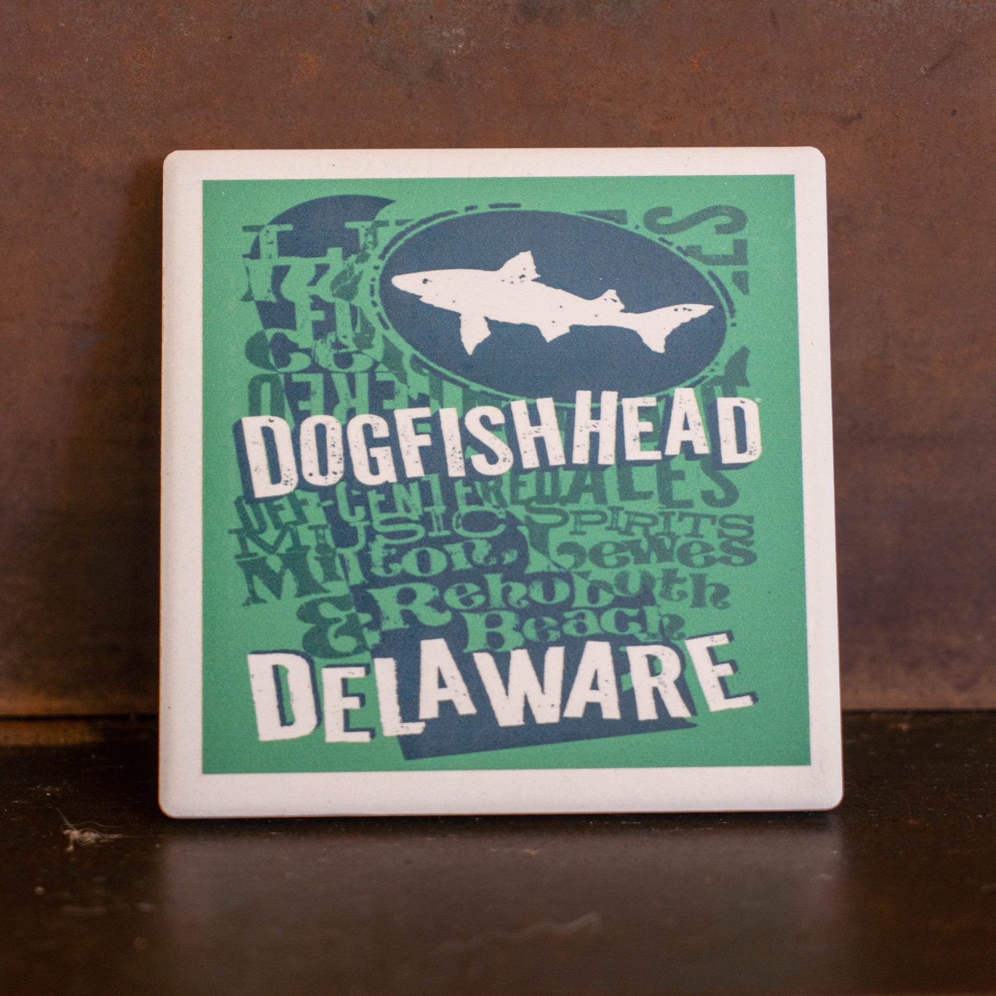 Introducing the Teal Delaware Ceramic Coaster by Paint the Town, Inc.—a rectangular accessory featuring a bold teal background with striking blue and white text that proudly showcases “Delaware” and your state pride. This eye-catching piece is an ideal addition for craft beer lovers or anyone seeking a stylish tribute to Delaware’s vibrant culture.