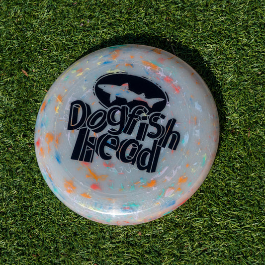 Grey frisbee with tie dye accents and a black Dogfish Head logo with "Dogfish Head" styled in 3-d block text laying on grass
