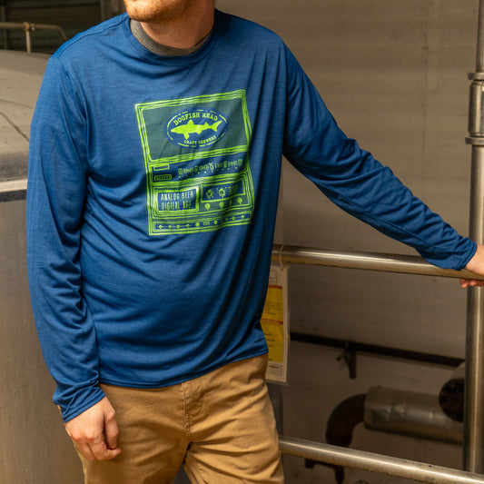 A man in a Patagonia M Blue Long Sleeve Runner featuring a bright green graphic design leans against a metal railing in an industrial indoor setting.