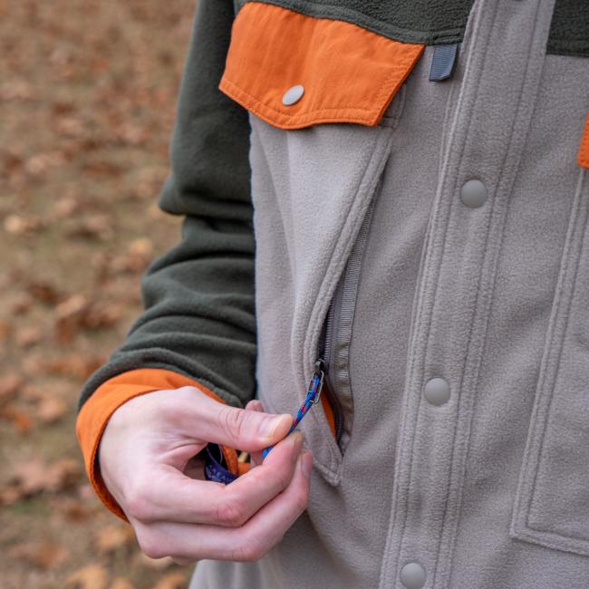 A person wearing a Patagonia M Grey Two Pocket Button Down is unzipping a side pocket. Fallen leaves are scattered on the ground in the background.