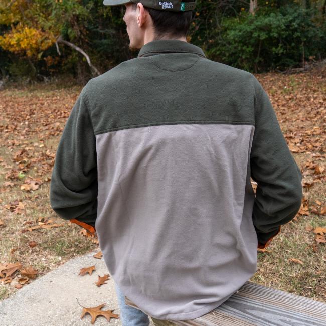 A person wearing a Patagonia M Grey Two Pocket Button Down and a cap sits on a wooden bench outdoors, facing away, surrounded by fallen leaves and autumn trees.