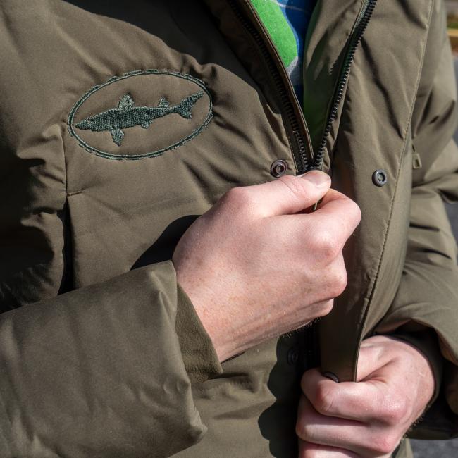 A person zips up the Patagonia M Olive Green Glacier Parka, showing only their hand and part of the windproof insulated jacket.