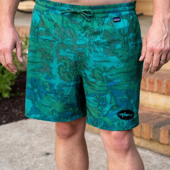 A person wearing Patagonia M Palm Tree Hydropeak Swim Trunks stands outdoors on a concrete surface near steps.