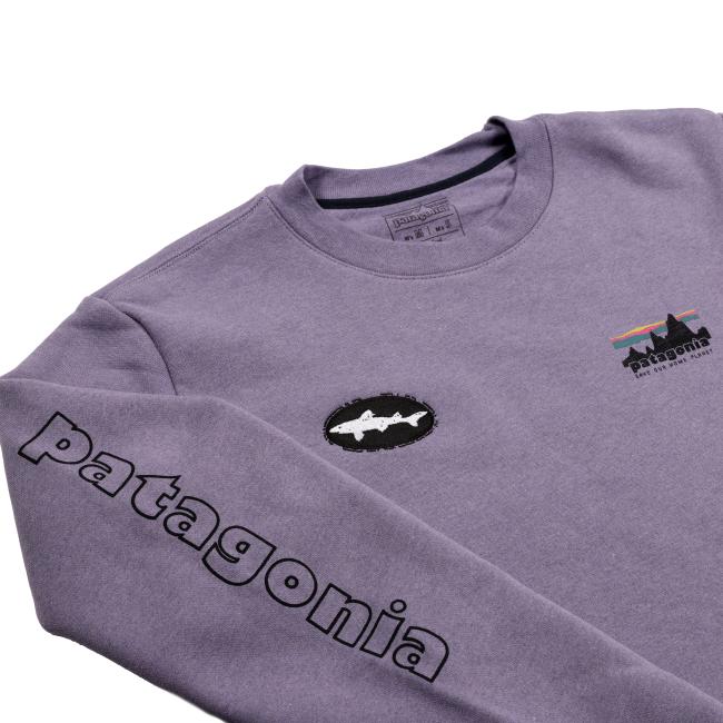 The Patagonia Purple Uprisal Crew Sweatshirt is a heavyweight crew with a black Patagonia print on the sleeve, a fish logo patch on the chest, and a multicolored Patagonia logo with fish graphic on the upper left chest.