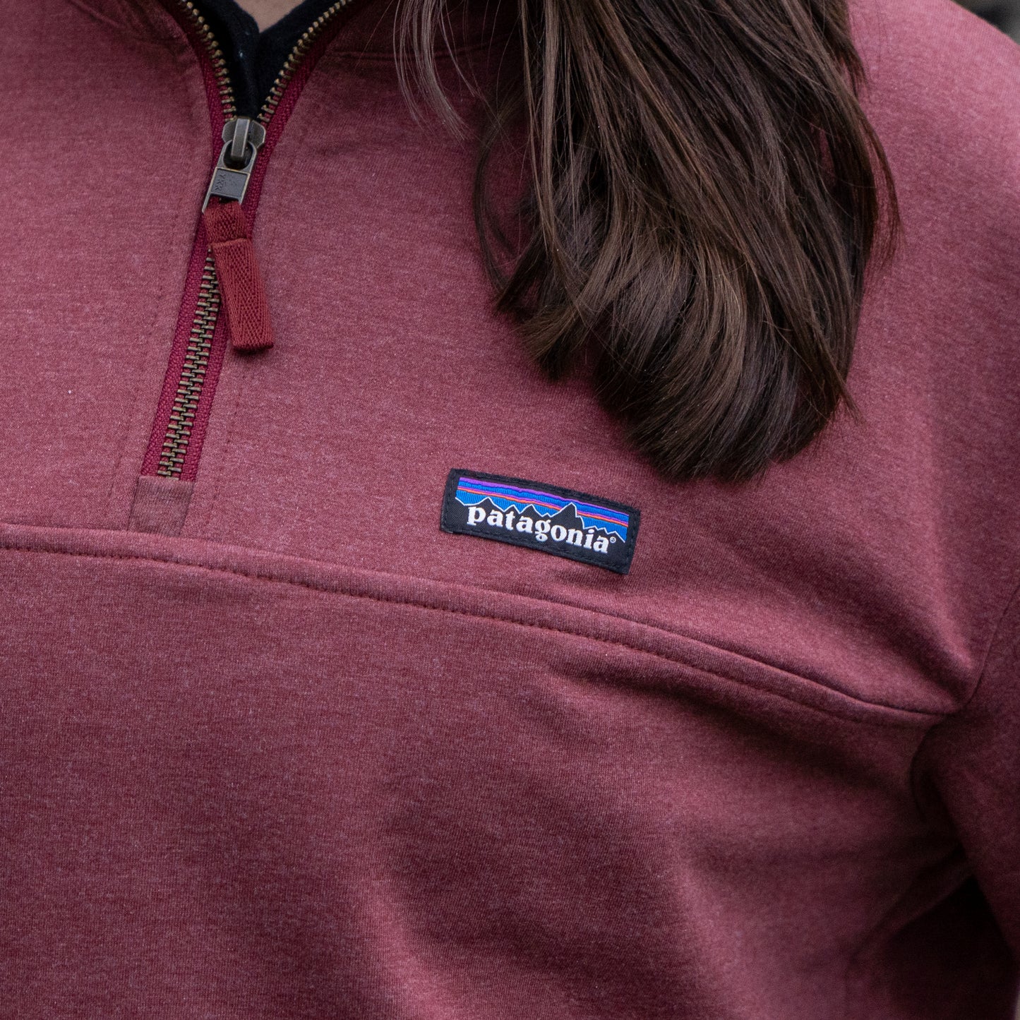 A person is shown from the upper torso up, wearing a Patagonia W Deep Red Ahnya Quarter Zip Pullover with the Patagonia logo patch visible on the chest.