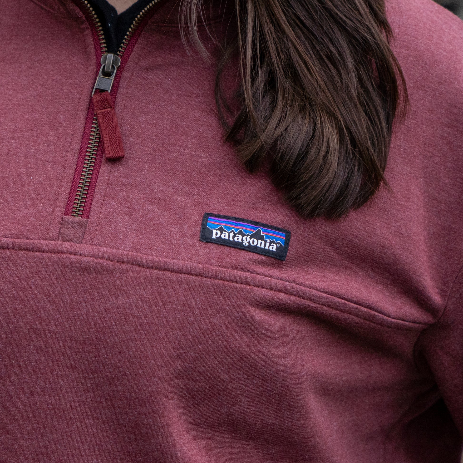 A person is shown from the upper torso up, wearing a Patagonia W Deep Red Ahnya Quarter Zip Pullover with the Patagonia logo patch visible on the chest.